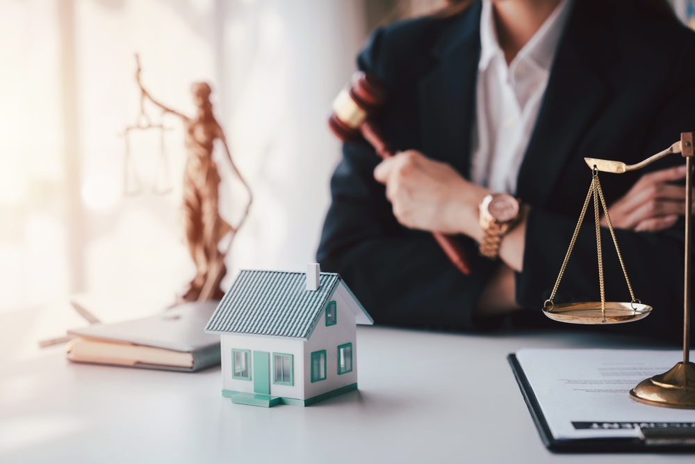 A professional adult Asian woman lawyer in suit offering legal services for real estate with a house model and justice scales representing law and consulting.