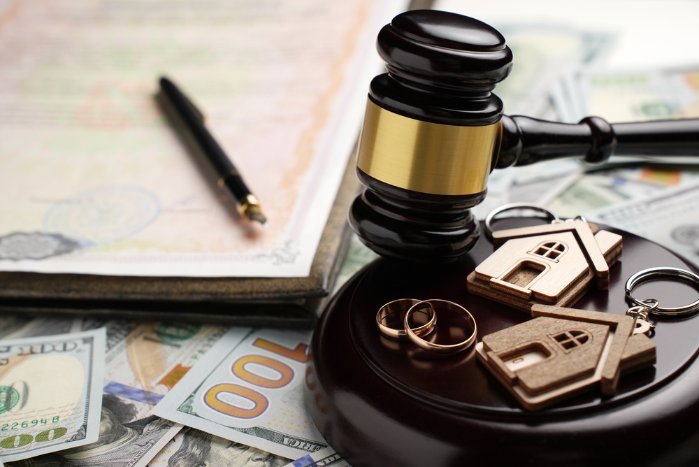 Property Division in Divorce and Marital Law Concept. Gold wedding rings, wooden house model, and a judge gavel on legal paperwork and US currency.