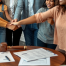 A diverse family is holding hands in a cozy office, with legal documents laid out on the table.