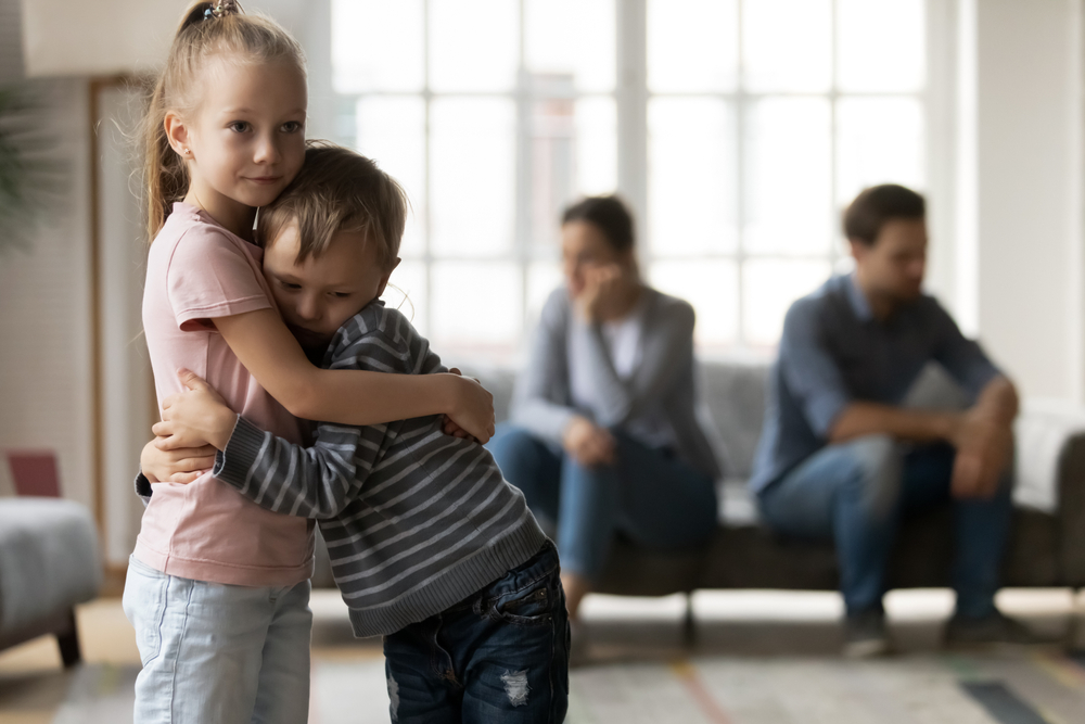 Upset little girl and boy, sister and brother hugging, suffering from parents quarrel close up, family conflict, offended mother and father ignoring each other after argument, children and divorce.