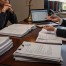A concerned couple sits at a desk with their lawyer, surrounded by legal documents, discussing divorce and immigration issues.