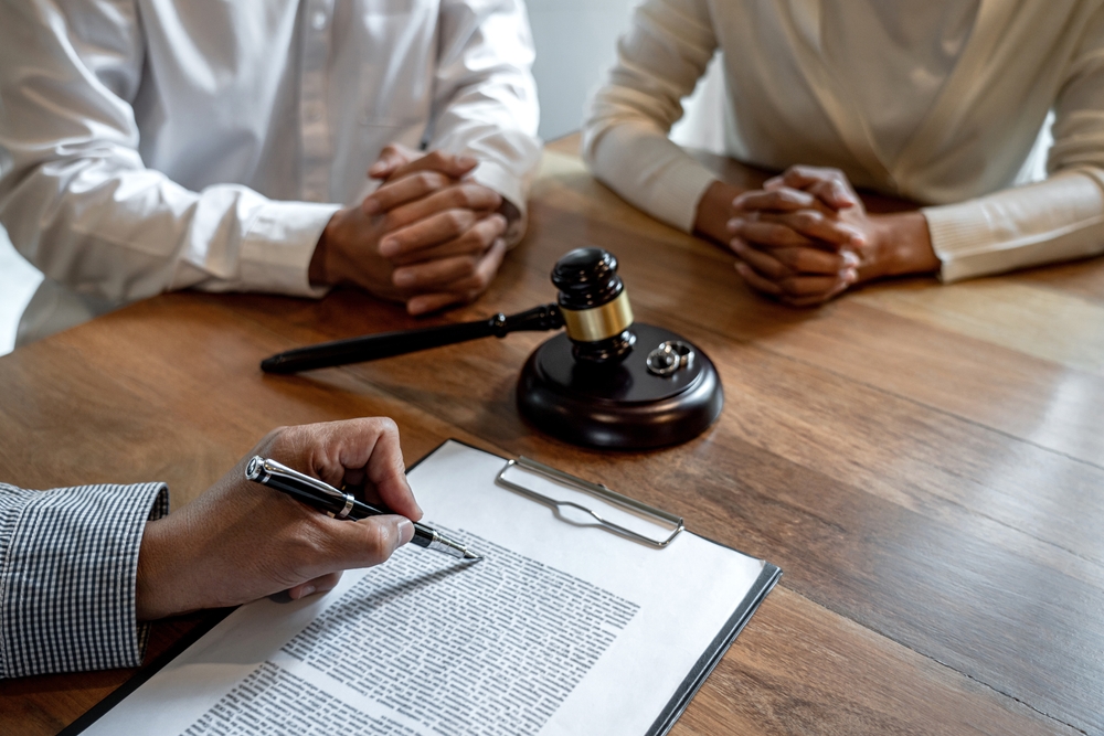 Unhappy divorce couple having conflict, husband and wife during divorce process with senior male lawyer or counselor and couple signing decree of divorce contract in lawyer's office.