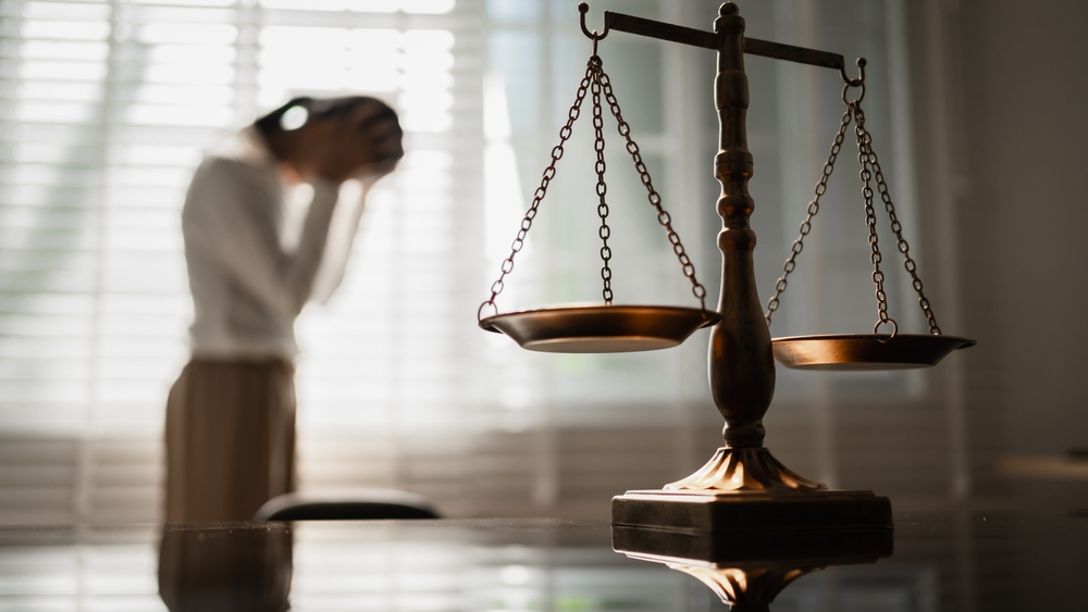 The scales of justice stand in focus while a woman seeks counsel, symbolizing the legal protection of women's rights, gender equality, safety from domestic violence, and the pursuit of fair justice.