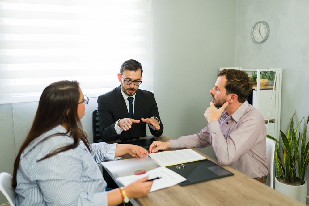 Attorney mediating between a distressed couple, reviewing legal documents and discussing separation terms at an office meeting