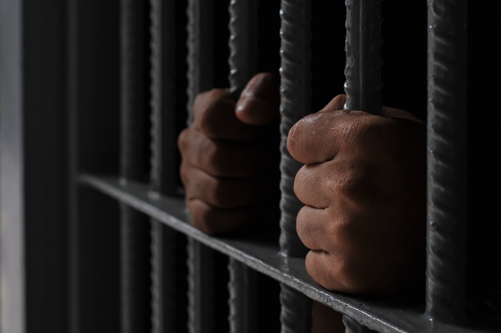 prisoner's hands behind bars with black background