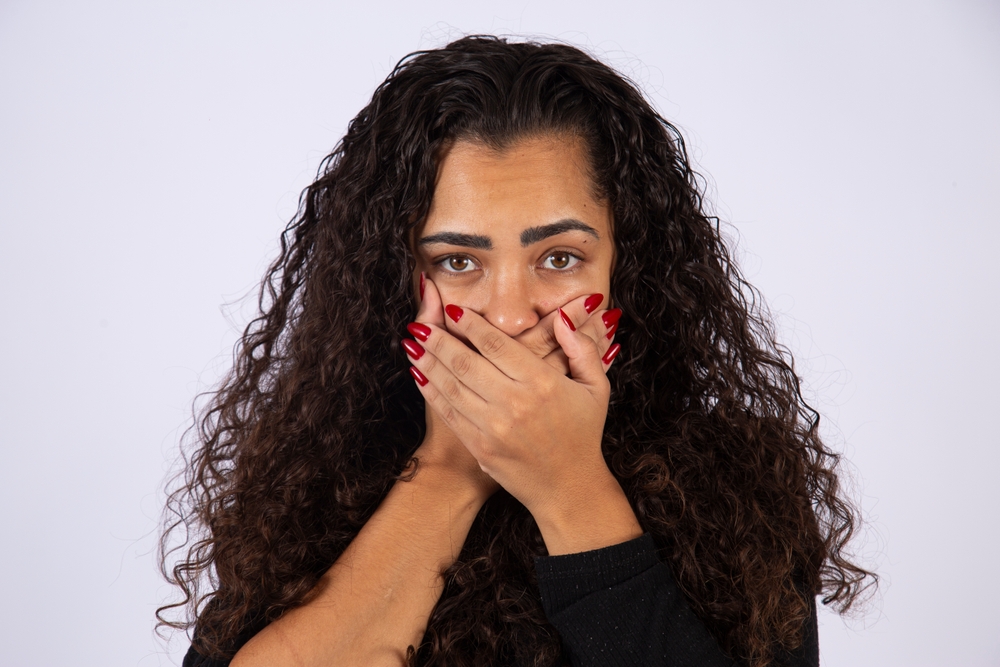 Brazilian woman, curly hair, fear, domestic violence, fight against feminicide. Hands over mouth, silence.