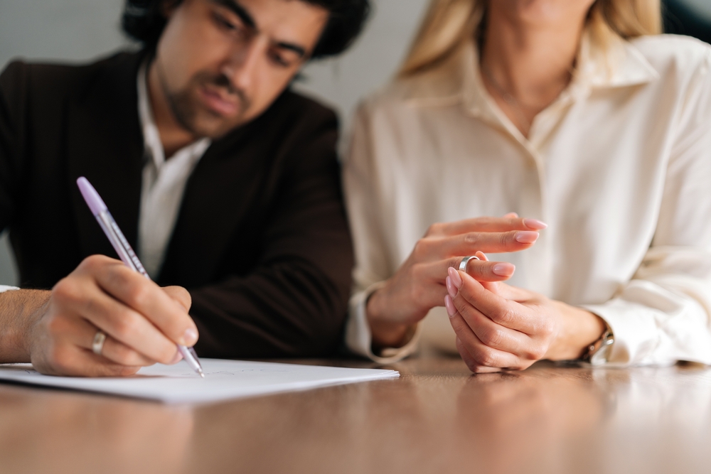 Cropped shot of sad spouses couple signing decree papers getting divorced in lawyers office at desk