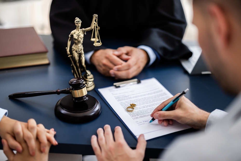 Young couple, one Caucasian and one Hispanic, consulting with a lawyer in court to sign a divorce agreement document.