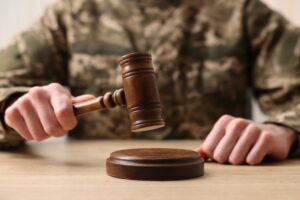 Law concept. Man in military uniform with gavel at wooden table, closeup