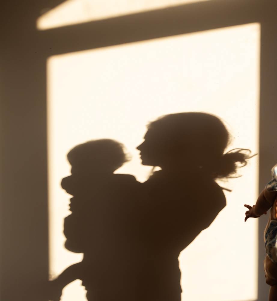 Silhouettes of a mother and baby on a wall, shadows of people illuminated by the sun.