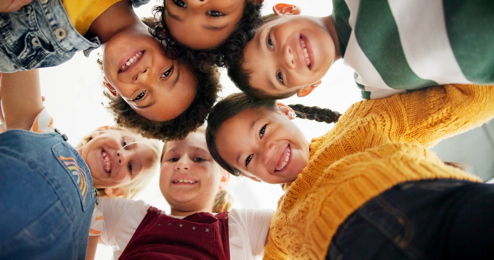 Huddle, support and happy children in school for education, community or development. Low angle, diversity and group of friends with smile in playground for solidarity, teamwork or playing together
