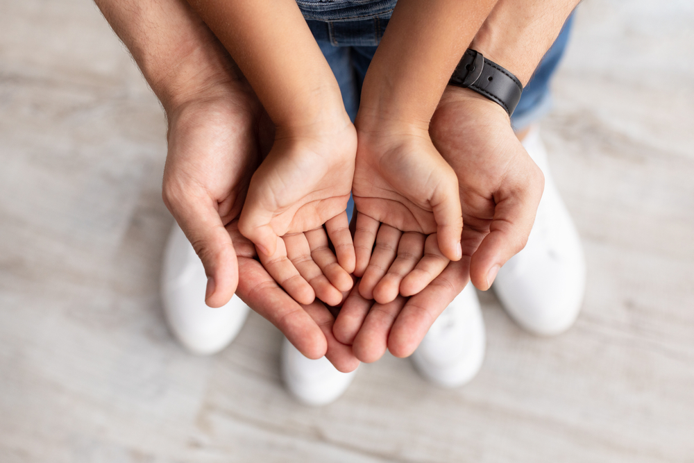 Cropped close up above top view of caring man holding girl's palms in hands, spending free time with daughter together at home.
