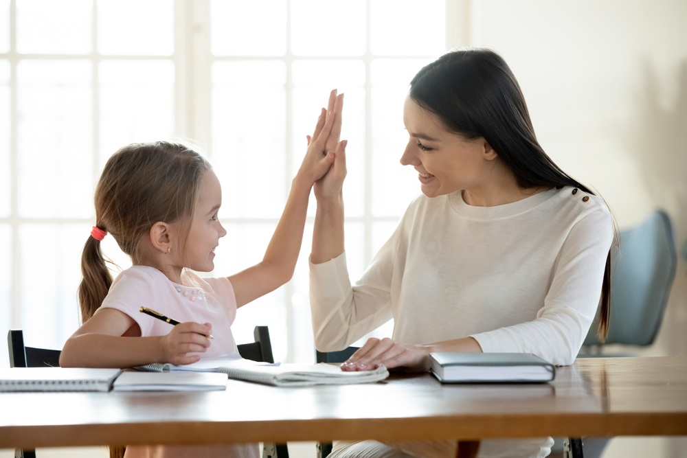 Joyful small daughter giving high five to satisfied with homework results mother.