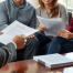 A smiling couple and a same-sex couple sitting with a professional lawyer in a well-lit office, reviewing legal documents.