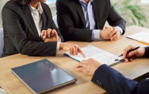 Cropped shot of two people business clients pointing fingers at a paper contract agreement on an office desk to clarify information, ask a question, or point at a mistake in the document