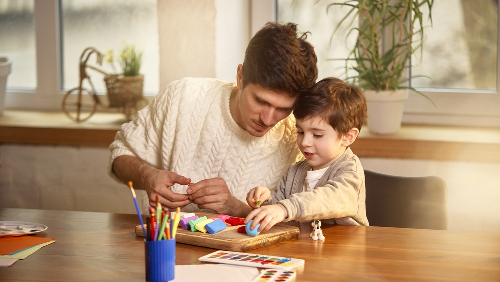 Father and young son concentrating on clay modeling at wooden table.