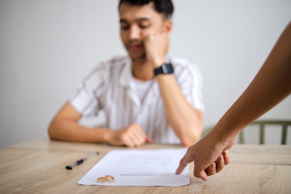 Wife Asking Her Upset Husband to Sign The Divorce Agreement Paper in Lawyer Office