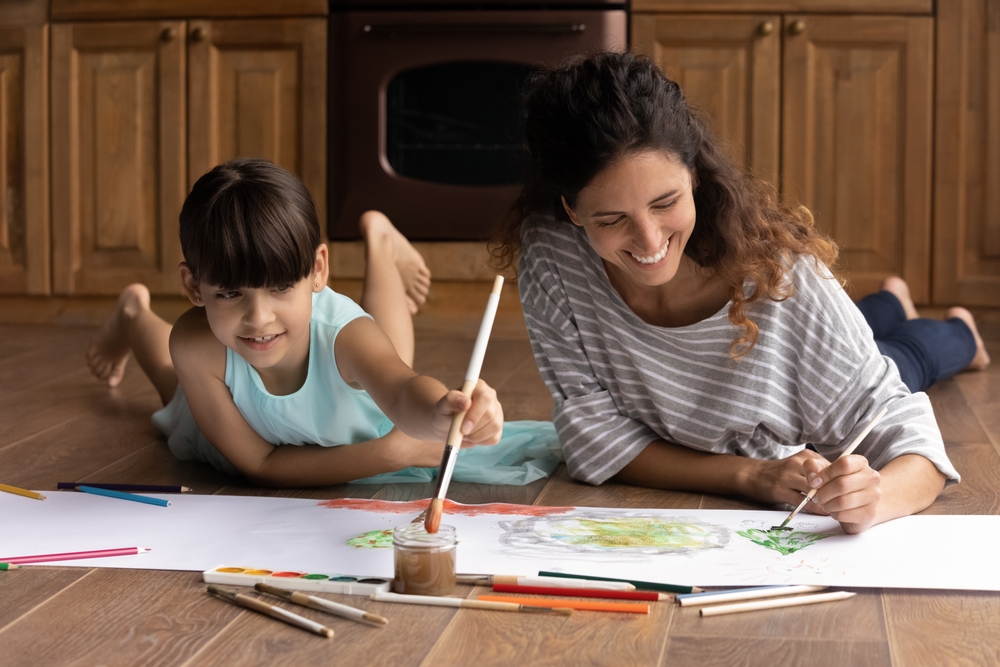 Quiet activity. Inspired hispanic woman babysitter engaged in drawing colorful picture with little preteen age girl.