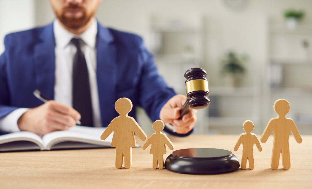 In family court, a lawyer delivers a verdict on divorce proceedings, wielding a gavel, beside wooden family figurines, symbolizing legal judgement regarding custody, children, and justice.