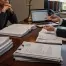 A concerned couple sits at a desk with their lawyer, surrounded by legal documents, discussing divorce and immigration issues.